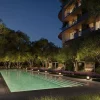 Rendu de la piscine des Aman Residences Beverly Hills la nuit, bordée d'oliviers et de cabanas, au pied d'une tour du complexe One Beverly Hills