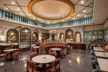 La salle du Café Alice au Roosevelt New Orleans, avec plafond à treillage vert, papier peint botanique, tables en marbre et banquettes de velours