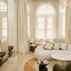 Salon d'une suite du Delano London, à Londres, canapé blanc arrondi et fenêtres cintrées voilées