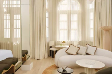 Salon d'une suite du Delano London, à Londres, canapé blanc arrondi et fenêtres cintrées voilées