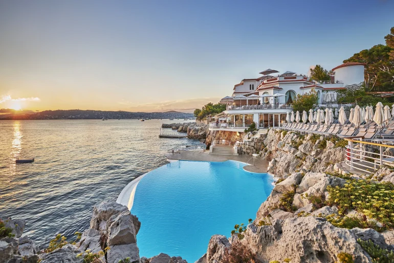 La piscine d'eau de mer taillée dans le roc de l'Hôtel du Cap-Eden-Roc au coucher du soleil, face à la baie de Juan-les-Pins