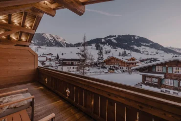 Vue depuis un balcon en bois de l’hôtel Fouquet’s Gstaad sur les chalets enneigés et les sommets