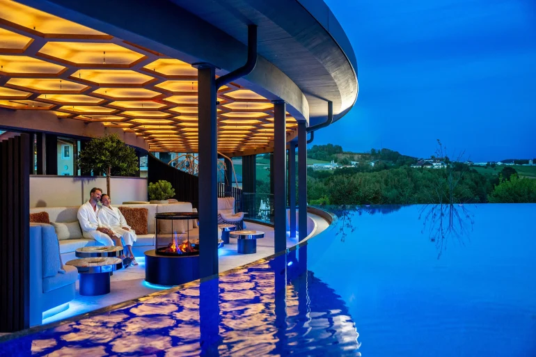 Sky-Lounge du Wellness- & Sporthotel Jagdhof à Röhrnbach, feu décoratif au bord du Sky Infinity-Pool en granit à la tombée de la nuit