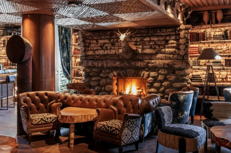 Le Bar du Lodge du Lodge Park à Megève, salon en rondins avec cheminée de pierre, Chesterfield en cuir et trophée de cerf