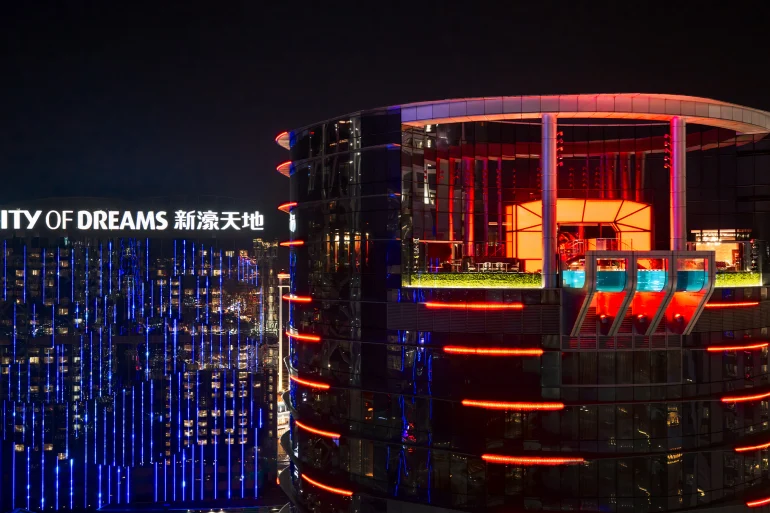 La tour de l'hôtel REM illuminée de rouge la nuit, à City of Dreams Macao, avec la piscine transparente de The Lair à son sommet