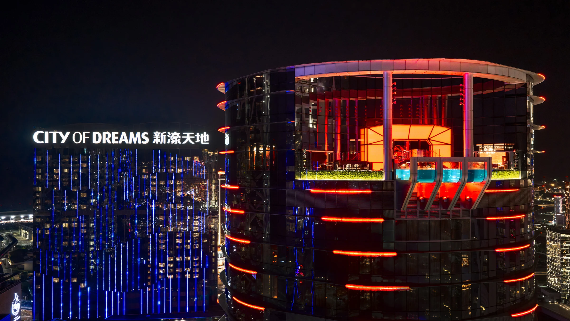 La tour de l'hôtel REM illuminée de rouge la nuit, à City of Dreams Macao, avec la piscine transparente de The Lair à son sommet