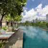 La piscine extérieure à débordement de The Den Bengaluru, LXR Hotels & Resorts, bordée de transats et de frangipaniers face aux tours de Whitefield