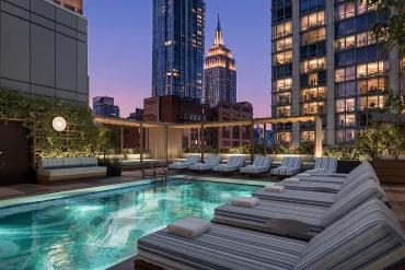 Rendu de la piscine extérieure sur le toit du Viceroy Park Avenue à New York, transats rayés face à l'Empire State Building au crépuscule