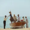 Scène de la série Netflix Le Problème final : arrivée en barque sur une plage de la Costa Brava, groom et clients en costumes de 1959