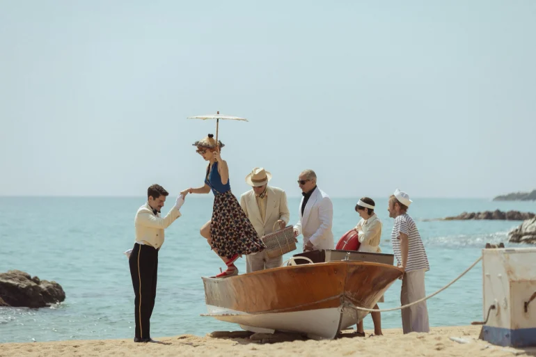 Scène de la série Netflix Le Problème final : arrivée en barque sur une plage de la Costa Brava, groom et clients en costumes de 1959