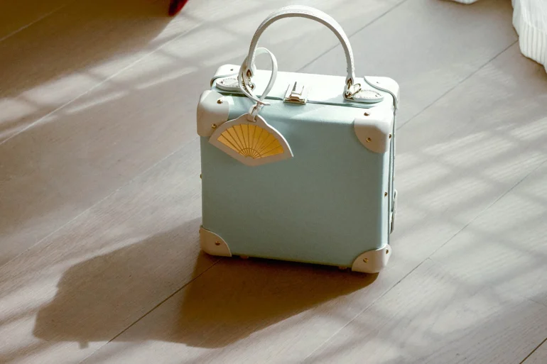 Le London Square Mandarin Oriental x Globe-Trotter en vert céladon, cuir ivoire et charm en éventail, posé sur un parquet