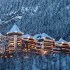 L'hôtel The Alpina Gstaad illuminé un soir d'hiver, ses tours coiffées de neige au-dessus de la forêt, à Gstaad en Suisse