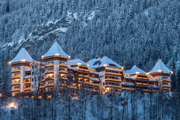 L'hôtel The Alpina Gstaad illuminé un soir d'hiver, ses tours coiffées de neige au-dessus de la forêt, à Gstaad en Suisse