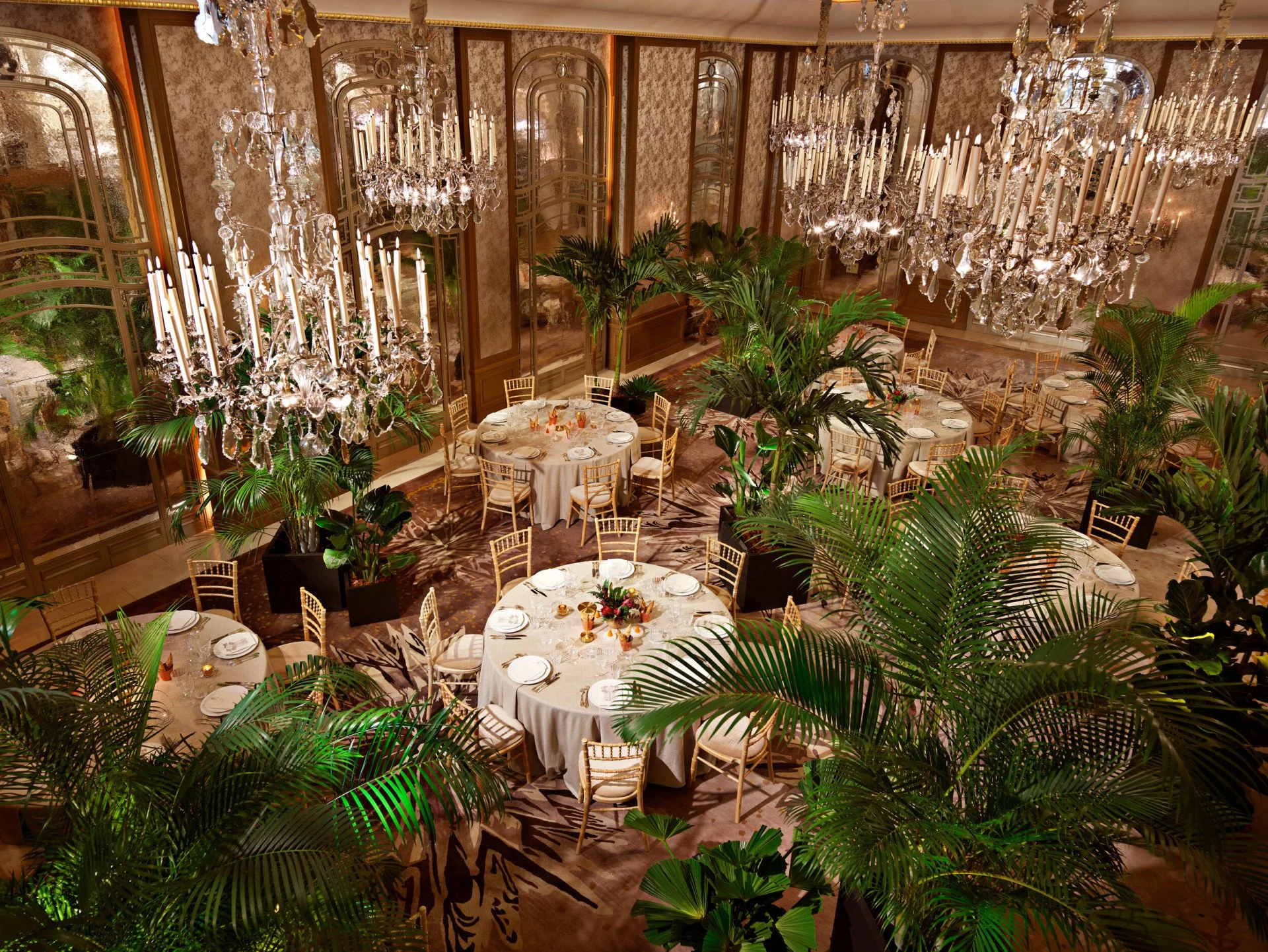 Le salon Haute Couture du Plaza Athénée, lustres de cristal, palmiers et tables rondes dressées pour un dîner