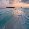 Un banc de sable blanc s'avance dans un lagon turquoise des Maldives au coucher du soleil, image officielle de Rosewood Ranfaru