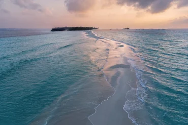 Un banc de sable blanc s'avance dans un lagon turquoise des Maldives au coucher du soleil, image officielle de Rosewood Ranfaru