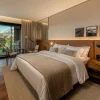 Chambre de The Almer Porto Alegre, bois naturel, baie vitrée sur la végétation du Country Club