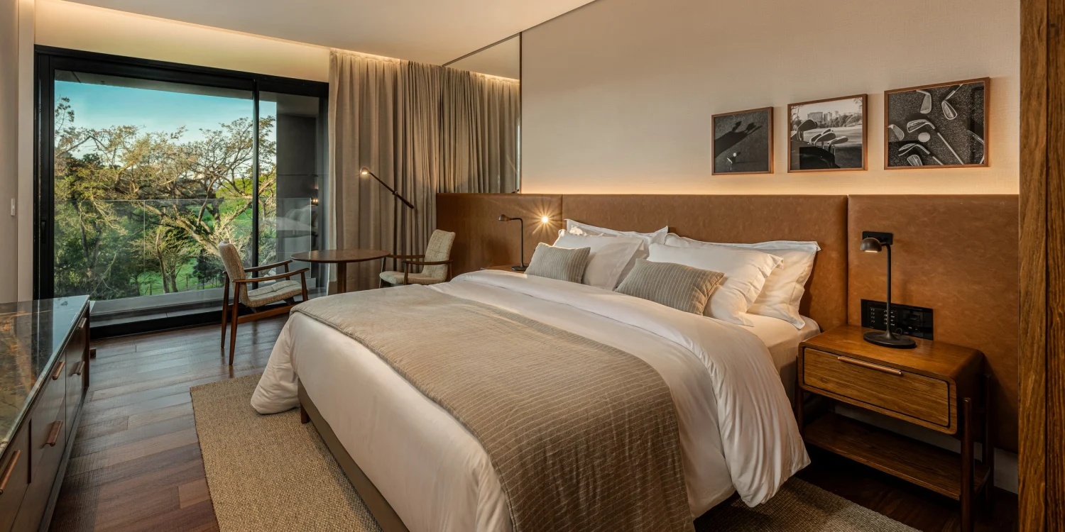 Chambre de The Almer Porto Alegre, bois naturel, baie vitrée sur la végétation du Country Club