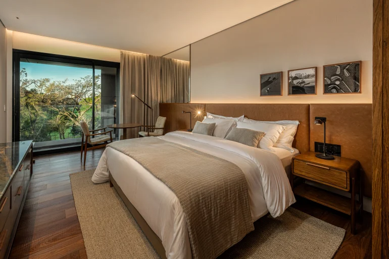Chambre de The Almer Porto Alegre, bois naturel, baie vitrée sur la végétation du Country Club